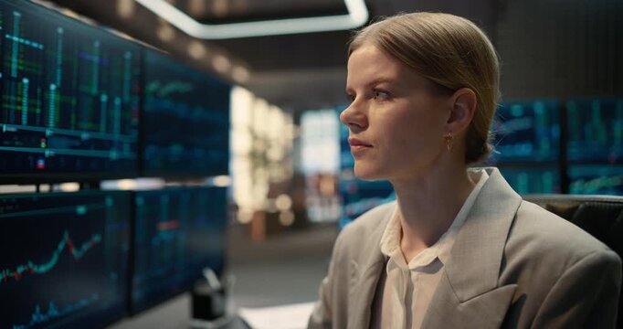 Zoom in Portrait of Female Trader Sits at a Desk Reviewing Stock Exchange Data, Financial Charts and Market Indices on Computer Screens, Analyzing Investment Trends and Capital Growth Opportunities.