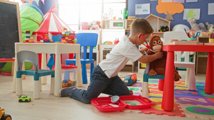 Boy kneeling, holding a toy stethoscope and medical kit with hands on alphabet foam mat in preschool  playful imagination. © Krakenimages.com