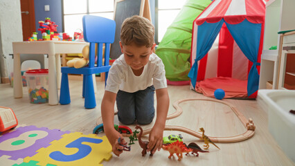 Boy kneeling and reaching with hand toward toy train on wooden floor in building playroom with tent, chair and foam puzzle mat  imaginative play joy. © Krakenimages.com