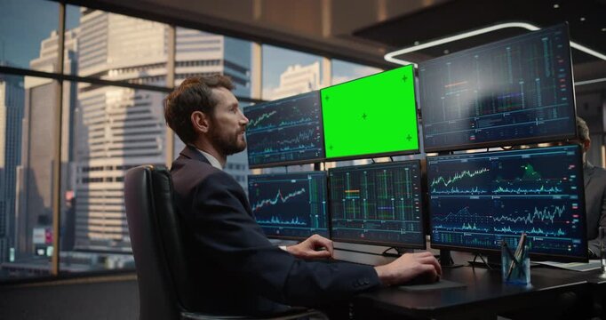 Male Stockbroker Works at Desk Analyzing Stock Exchange Data on Screens With Green Screen Chroma Key Monitor, Monitoring Market Trends, Investment Analytics and Capital Growth in Office