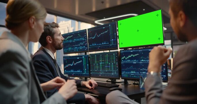 Team of Brokers Talk at Desk Reviewing Stock Exchange Data on Green Screen Chroma Key Monitor, Discussing Financial Charts, Investment Analytics, Market Trends and Capital Growth in Office