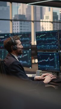Vertical Screen. Confident Male Trader Wearing Headset Talks With Client While Analyzing Stock Market Data and Financial Charts at Desk, Executing Trades and Capital Growth Strategy.