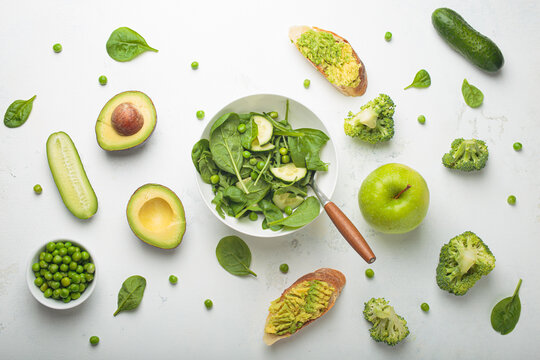 Fresh salad bowl, avocado toasts, raw green vegetables fruit white background top view, diet