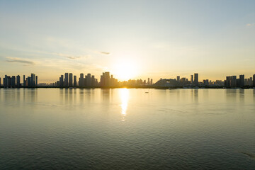 The sun rises over the modern city skyline of Wuhan China reflecting beautifully on the calm water surface of the river during a clear morning © AS_SleepingPanda