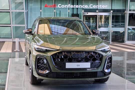 New olive green Audi Q5 Sportback SUV parked in front of the Audi Conference Center glass facade entrance at Munich Airport, Germany, premium automotive branding and modern travel concept.