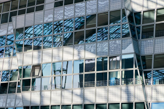 Close up abstract view of the modern glass facade of Munich Airport Center in Germany, featuring unique angular geometric panels, metallic grid frames and protective mesh details.