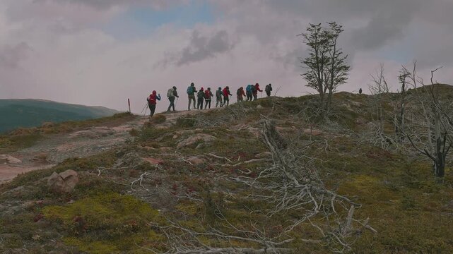 A line of hikers with backpacks hiking up a ridge line on a cloudy day, W Trek, Patagonia, Chile