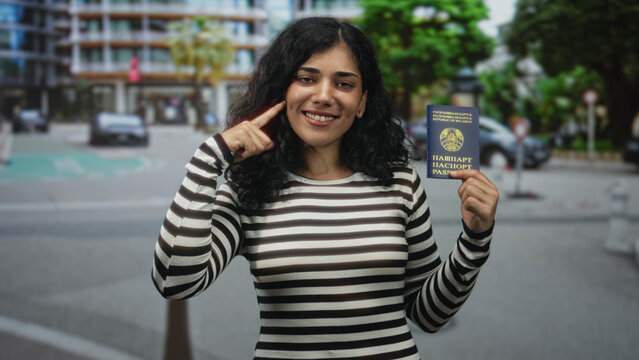 Young woman holding belarus passport and pointing finger to temple on a city street; identity confidence travel.
