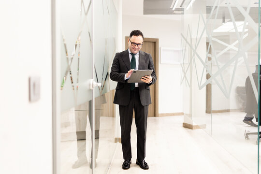 Full shot of a lawyer or business professional, aged 40-50, in a suit, looking at a tablet in a modern office. Concept of mature businessmen.