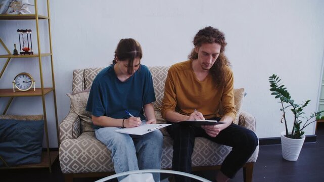 A young man with curly long hair and woman complete a mental health questionnaire while sitting in armchairs during a professional appointment