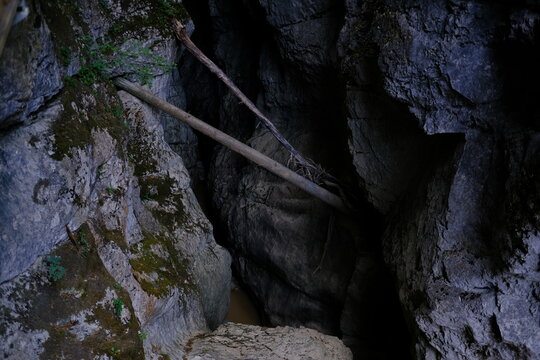 Dark cave opening with wooden log and mossy rocks in mountain gorge