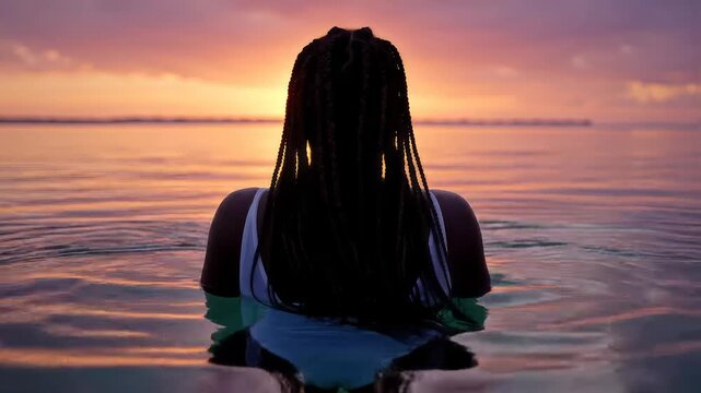 Woman relaxing in calm ocean water while watching a glowing sunset