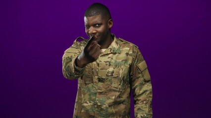 Soldier man in camouflage uniform beckons with fingers toward camera, prominent hand visible against purple studio wall  pride duty. © Krakenimages.com