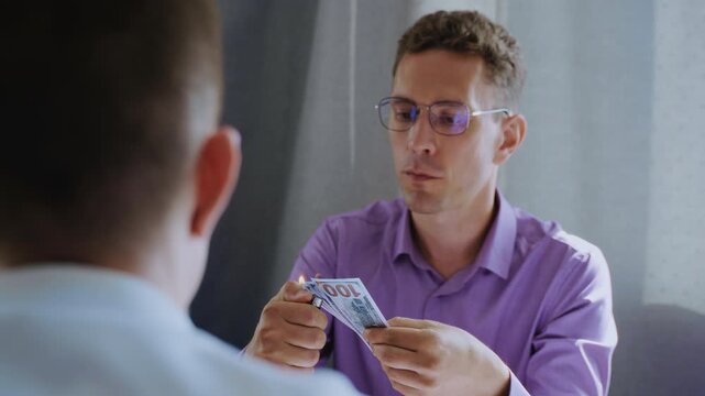 Businessman in an office burning a wad of one hundred dollar bills in front of a colleague