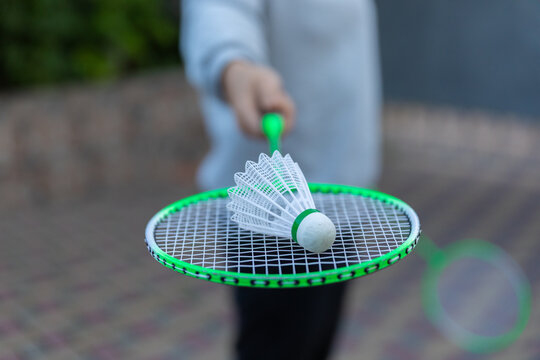 Close-up of a badminton racket and shuttlecock outdoors with a blurred background, perfect for sports, recreation, and fitness themes.