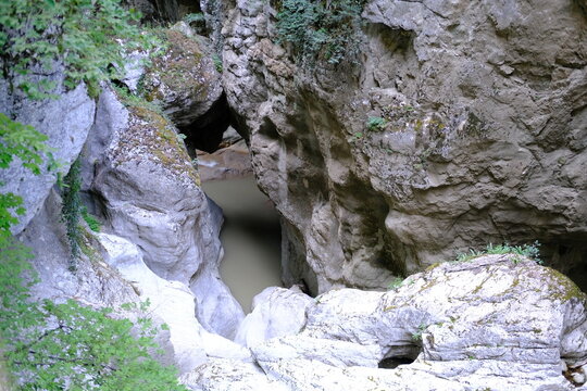 Rocky gorge with natural cave opening surrounded by cliffs and greenery