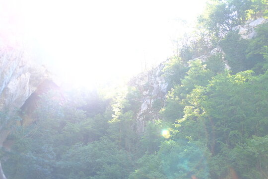 Sunlight flare over rocky forest landscape with bright overexposed sky