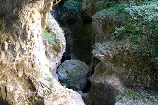 Narrow rocky canyon with mossy cliffs and dark cave entrance in nature