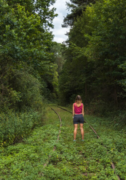 Back view of a woman standing on abandoned railway tracks in a lush green forest. Conceptual image of solo travel, future paths, and career decisions