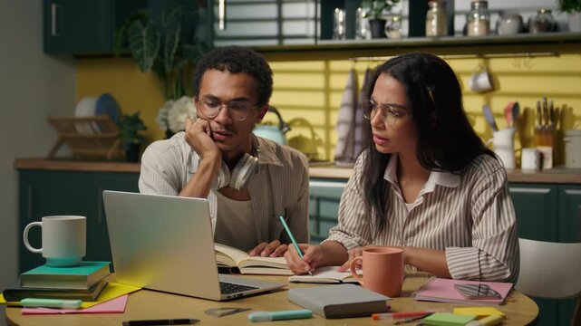 Multiracial African American man and Latina woman studying together at home using laptop students writing homework online class distant education university teamwork young freelancers teens at kitchen