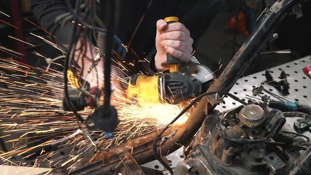An engineer in a garage is modifying a motorcycle, sawing and trimming off excess frame elements with a circular saw.