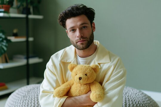 Young man holding a yellow teddy bear portrait in a cozy living room for background and wellbeing campaign design