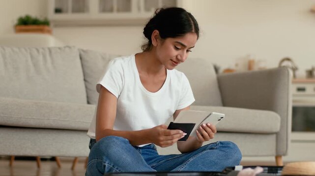 Smiling Hindu Indian woman at home preparing for trip vacation travel female Arabian girl browsing mobile phone ordering flight chatting booking hotel packing clothes suitcase tickets passport indoors
