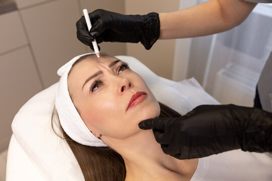 Close-up. Before the procedure for facial contouring or plastic surgery, female cosmetologist in black gloves carefully makes markings on the patient face. Time to prepare for a cosmetic procedure.