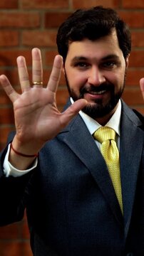 Showing numbers using fingers with confident expression, Indian Asian bearded ceo businessman in formal corporate attire demonstrating finger counting while standing in cozy office against brick wall
