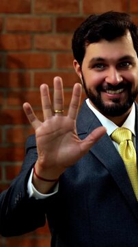 Showing numbers using fingers with confident expression, Indian Asian bearded ceo businessman in formal corporate attire demonstrating finger counting while standing in cozy office against brick wall