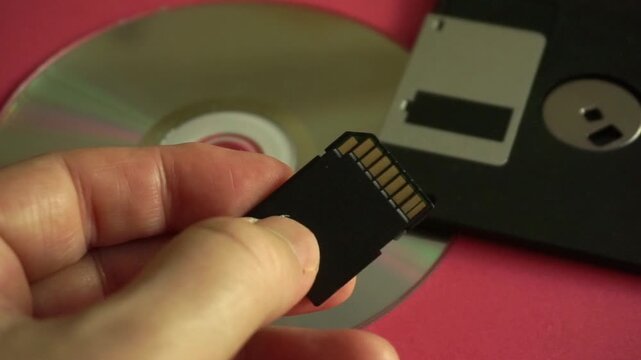 Human hand showing the difference between old and modern digital storage media over a pink background