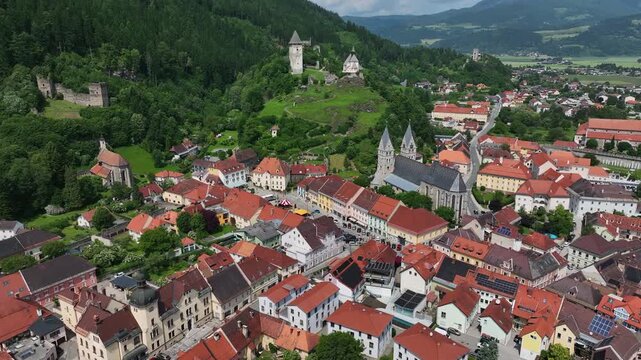 Summer drone footage showing medieval Friesach, old fortified walls, rooftops, towers, hills, serene atmosphere, warm daylight, gentle cinematic motion