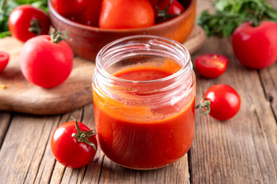Homemade tomato paste, puree, sauce or ketchup in a small glass jar. Tasty tomato preserves from fresh ripe red tomatoes, on a wooden background with fresh vegetables