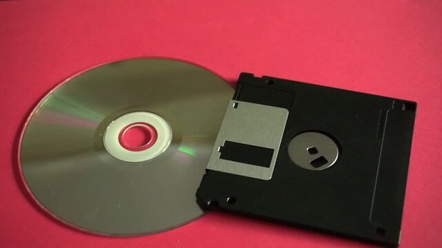 Conceptual comparison between an old floppy disk and a more recent compact disc on a red surface