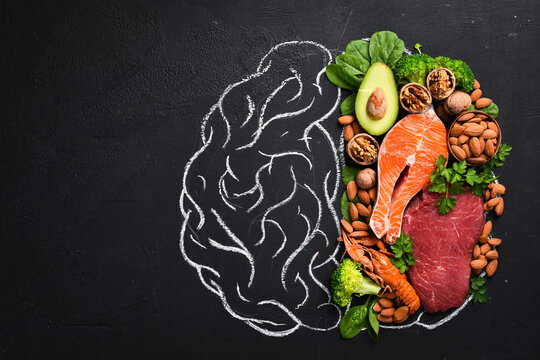 Concept of healthy food for the brain: fish, meat, nuts, vegetables and greens. Brain drawing with chalk on a blackboard. Top view. On a black background.