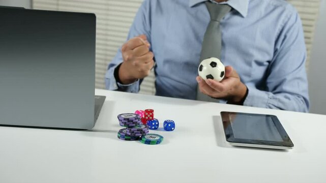 A happy and excited man sits at a computer desk holding a miniature football, feeling euphoric about winning a football bet, staring at the screen and celebrating the fantastic news, receiving the bes