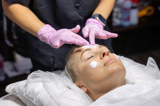 Cosmetic physician applies a professional facial cream during a skincare treatment, preparing the skin for the next stage of a cosmetic procedure in a beauty clinic.