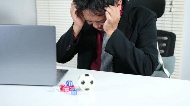 A young man loses a bet while gambling on soccer, facing failure and regret. He displays a depressed expression in front of his laptop, playing soccer and losing all his money, losing his gambling.
