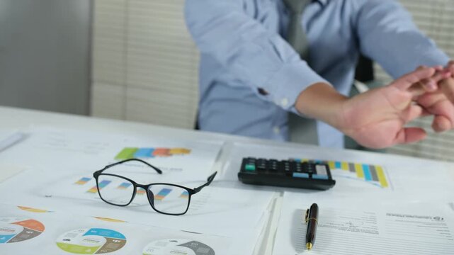 A young businessman stretches his arms while relaxing at his desk in a comfortable chair with his eyes closed, focused on his work. A tired-looking young businessman is resting in his office after com