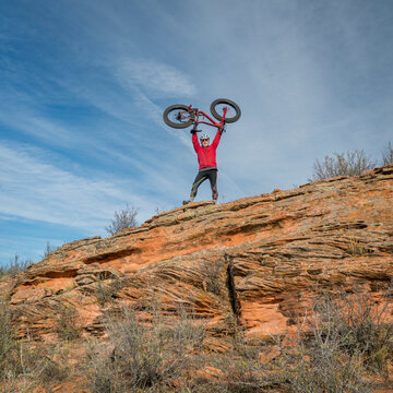 male rider lifting his fat bike on a sandstone cliff in Colorado foothills, fall scenery
