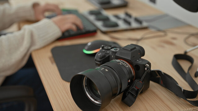 Woman photographer with camera on wooden desk typing on keyboard beside mouse and tripod in studio; creative focus.