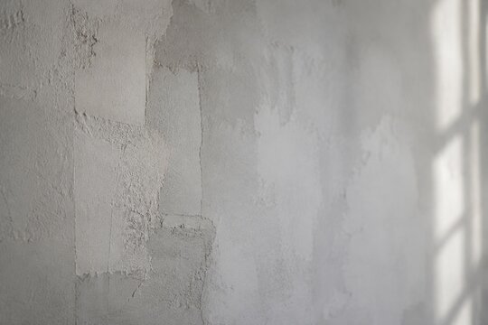 A grey-white wall with interwoven textures of old and new plaster repairs.