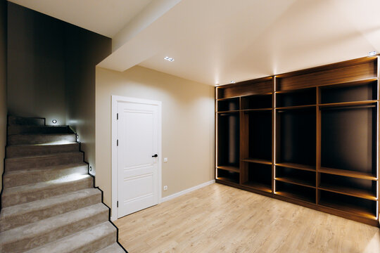 Finished basement entry with carpeted staircase, white landing door, and illuminated built-in wooden storage wall under warm recessed lighting in clean modern home interior