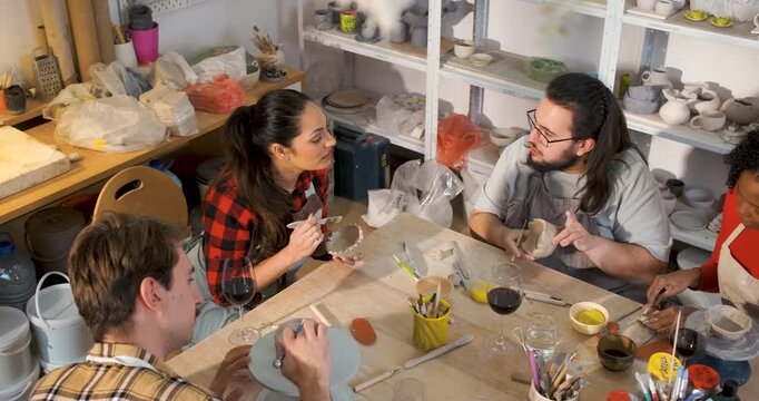 Diverse group of friends attending pottery class having fun making clay objects together.