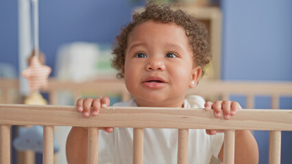 Little girl stands and grips crib rail with small hands in nursery building near mobile  tender curiosity warmth. © Krakenimages.com