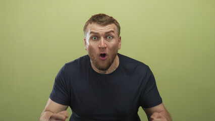 Fototapeta premium Young caucasian overweight man with raised fists, tongue out and bearded face cheering in studio with olive green background; excitement celebration win.