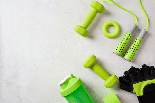 Assorted green sport equipment and workout accessories on the right side of a textured gray background with copy space. Flat lay.
