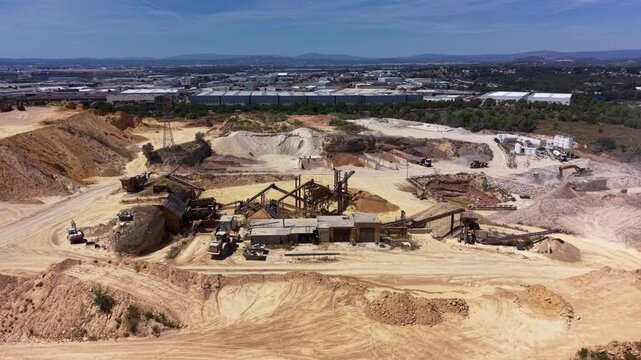 Aerial view of an active sand and gravel quarry featuring a crushing and screening plant, conveyor systems, stockpiled aggregate, industrial park and mountains in background