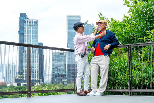 Couple Asian senior lgbtq men with one help to set up cloth of the other man who lean on iron railing in walking street park in big city and they look happiness together.