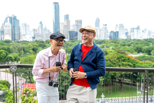 Asian senior lgbtq with colorful cloth stand and laugh together look like fun in front of park and city view in concept of happiness lifestyle in big city.